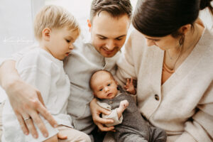 Familien Fotoshooting mit neugeborenem Baby. Das Baby wird in der Mitte der Familie gehalten, alle anderen kuscheln sich aneinander. Fotografiert von Kim Kärger.