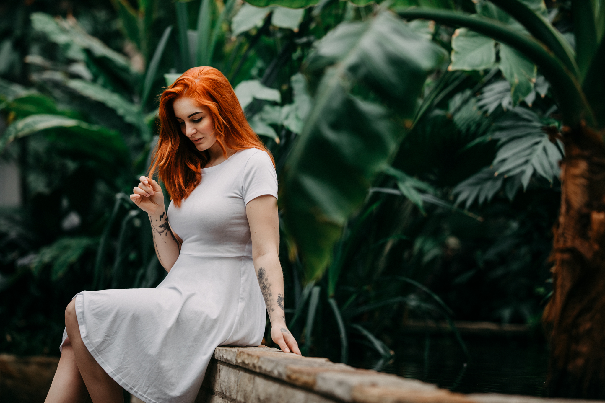 Kim Kärger in einem weißen Kleid sitzend auf einer Mauer im botanischen Gewächshaus von Hannover